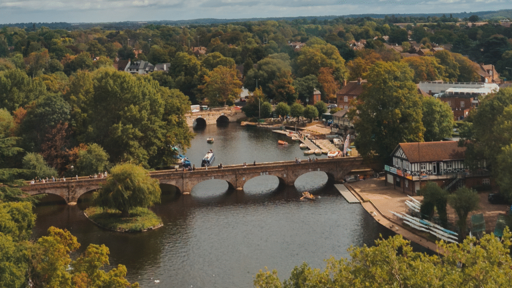 A view of Stratford Upon Avon looking over the river Avon, with a birdge and green and orange trees.